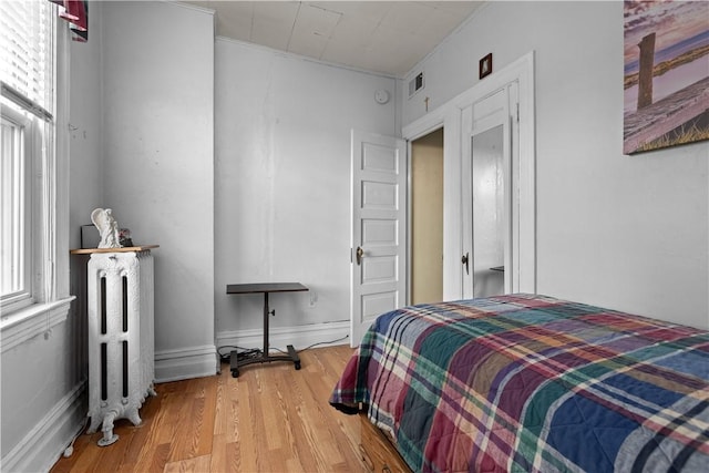 bedroom with visible vents, wood finished floors, and radiator heating unit