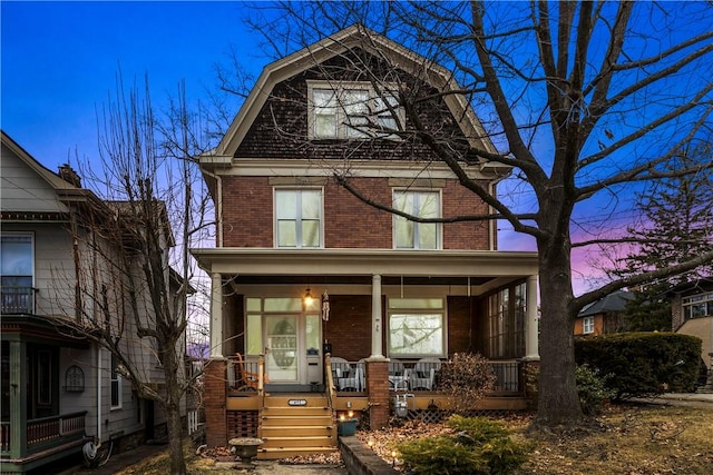 view of front of home with a gambrel roof, brick siding, and a porch