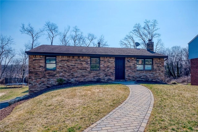 single story home featuring brick siding, a chimney, a front yard, and a trampoline