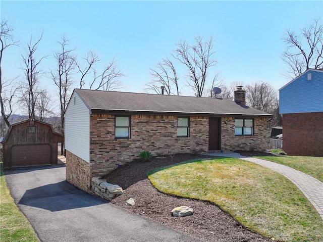 ranch-style home with brick siding, a detached garage, a front yard, a chimney, and an outbuilding