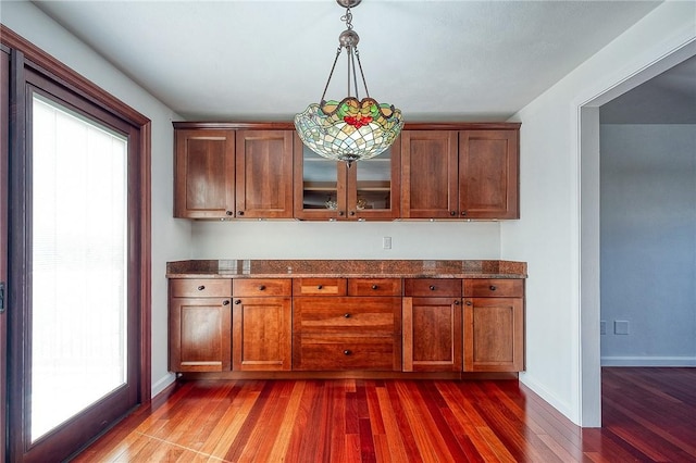 kitchen with dark stone countertops, baseboards, hanging light fixtures, dark wood-type flooring, and glass insert cabinets