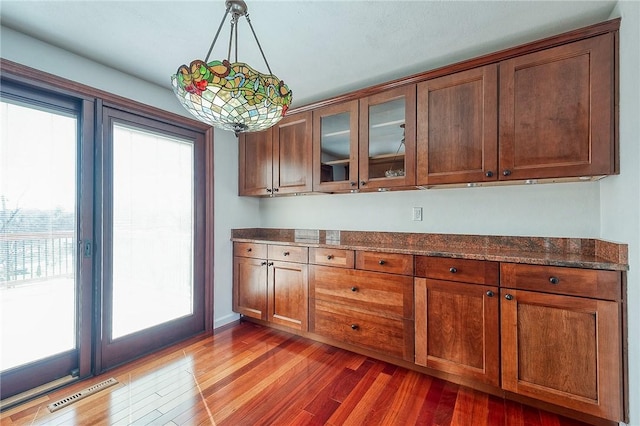 kitchen featuring visible vents, glass insert cabinets, pendant lighting, dark stone counters, and light wood-style floors