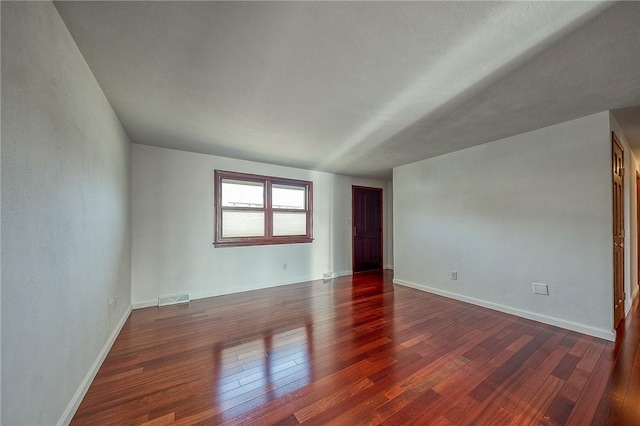 spare room with visible vents, baseboards, and dark wood finished floors