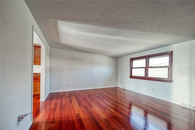 empty room with dark wood-style floors, visible vents, a textured ceiling, and baseboards