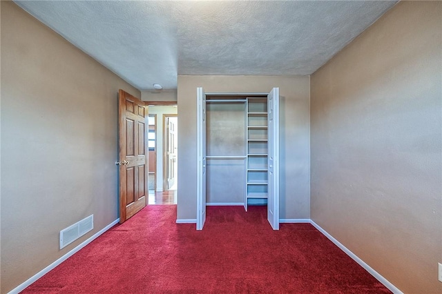 unfurnished bedroom featuring visible vents, baseboards, a closet, a textured ceiling, and dark colored carpet