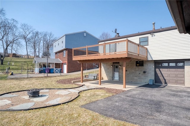 back of house featuring an outdoor fire pit, an attached garage, an outdoor structure, a deck, and a patio area