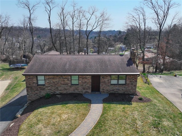 view of front of property with a front lawn, a trampoline, a shingled roof, brick siding, and a chimney