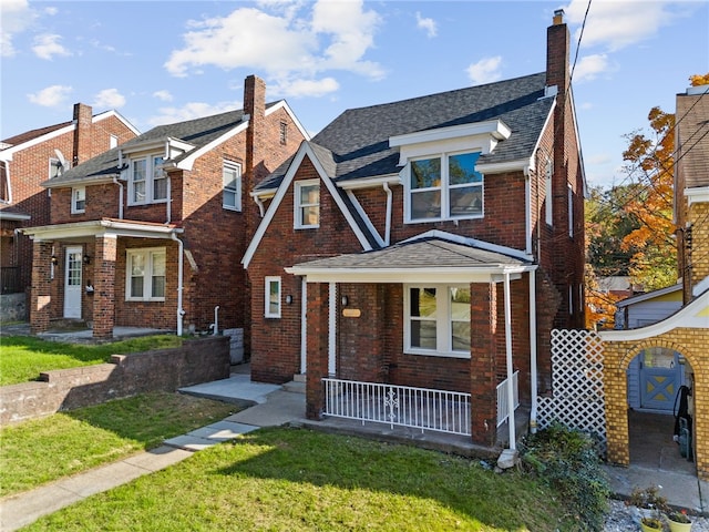 view of front facade with roof with shingles, covered porch, a chimney, a front lawn, and brick siding