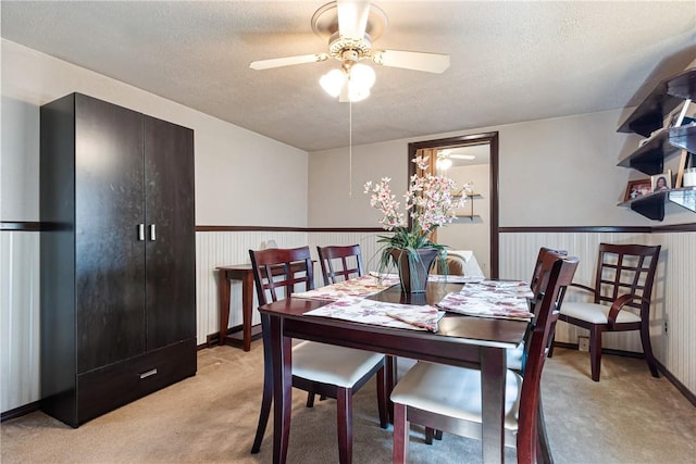 dining space featuring light colored carpet, a textured ceiling, ceiling fan, and wainscoting