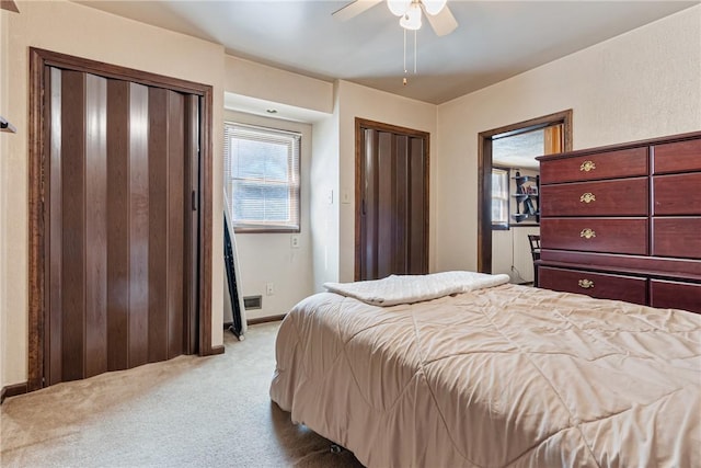 bedroom featuring carpet flooring, ceiling fan, two closets, and baseboards