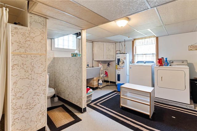 basement featuring a drop ceiling, washer and dryer, electric water heater, and baseboards