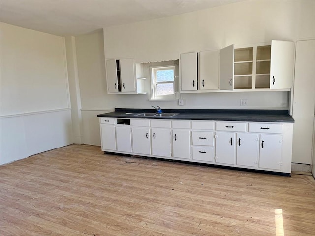 kitchen featuring dark countertops, white cabinets, light wood finished floors, and a sink