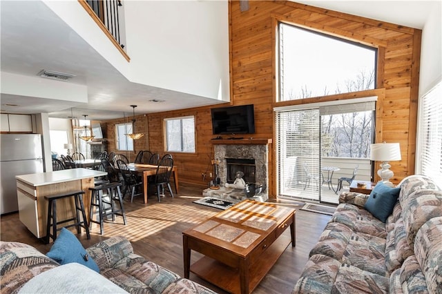 living area with a stone fireplace, visible vents, dark wood-style floors, and wood walls