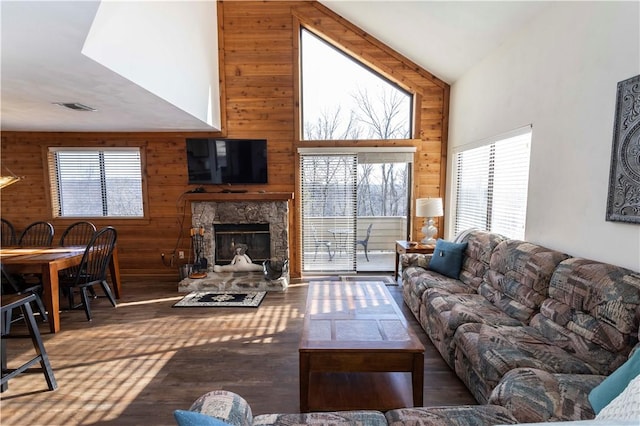 living room with a fireplace, visible vents, wood walls, and high vaulted ceiling