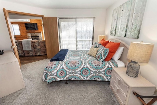 carpeted bedroom featuring a stone fireplace and wood walls