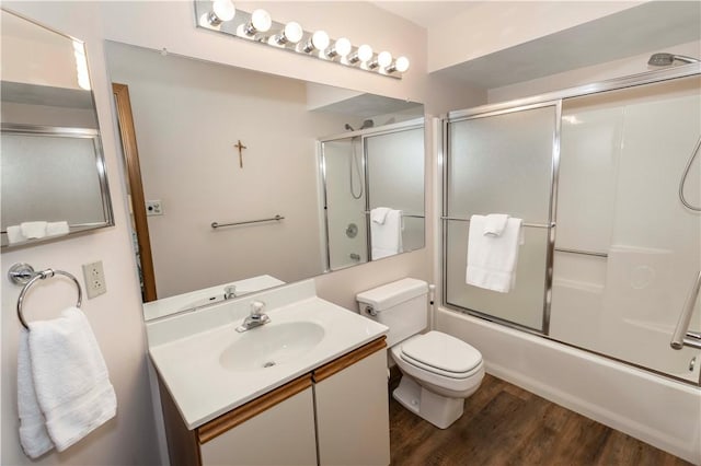 bathroom with vanity, toilet, wood finished floors, and shower / bath combination with glass door