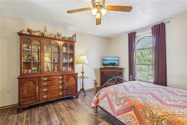 bedroom with baseboards, dark wood finished floors, a warm lit fireplace, a textured ceiling, and a ceiling fan