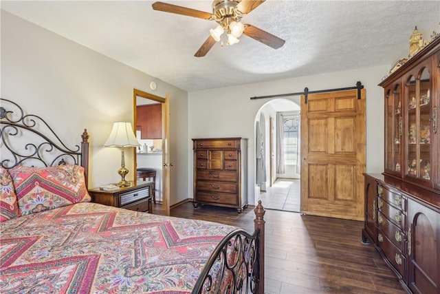 bedroom featuring ceiling fan, a barn door, arched walkways, a textured ceiling, and dark wood-style flooring