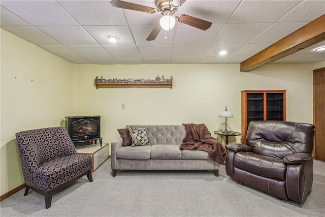 carpeted living room with baseboards, a drop ceiling, beam ceiling, a wood stove, and a ceiling fan