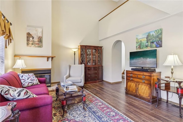 living area featuring baseboards, a fireplace, a high ceiling, wood finished floors, and arched walkways