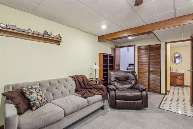 carpeted living room with baseboards, a drop ceiling, and a sink