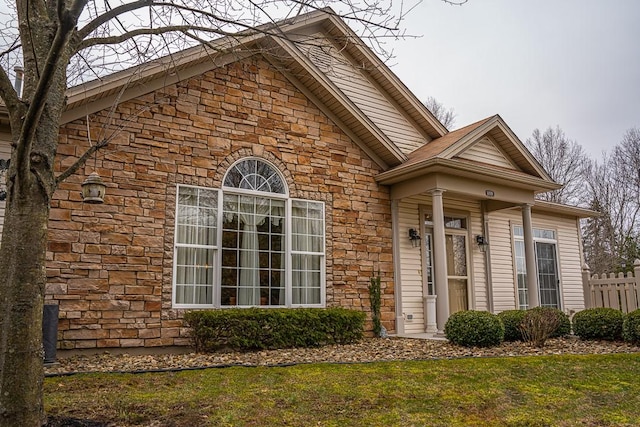 view of front of house with stone siding, a front lawn, and fence