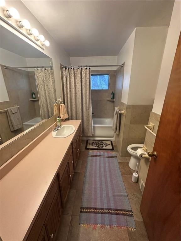 bathroom featuring tile patterned floors, toilet, shower / tub combo with curtain, tile walls, and vanity