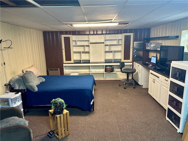 bedroom featuring a paneled ceiling, wood walls, and dark carpet