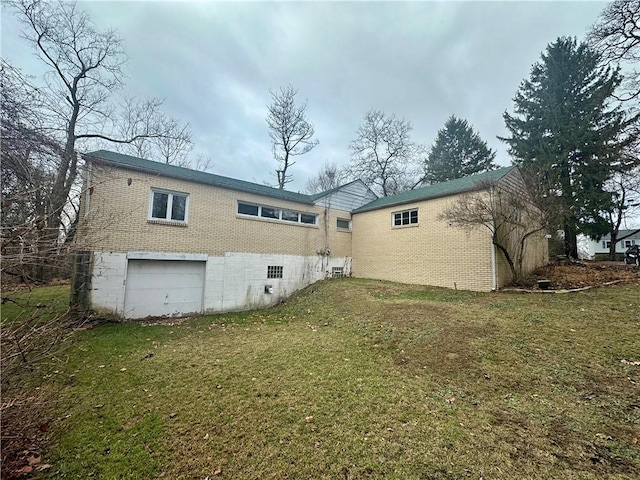 back of house with brick siding, a lawn, and a garage