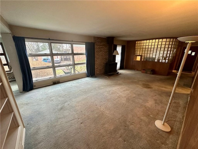 unfurnished living room with visible vents, a wood stove, and carpet