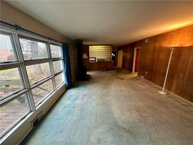 unfurnished living room featuring visible vents, a wood stove, wood walls, and carpet flooring