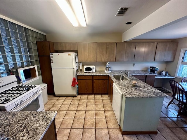 kitchen with a sink, visible vents, white appliances, and light stone counters