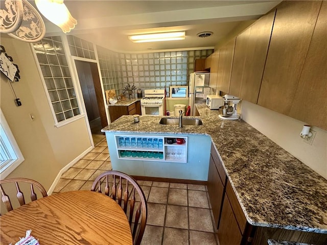 kitchen with visible vents, a sink, freestanding refrigerator, a peninsula, and white range with gas stovetop