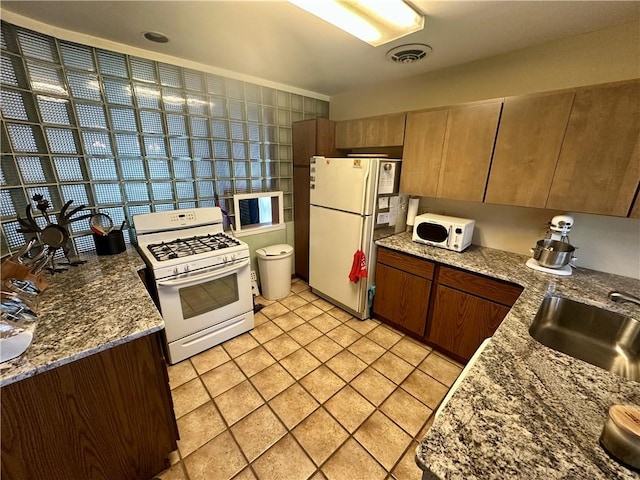 kitchen with white appliances, light tile patterned floors, visible vents, stone countertops, and a sink