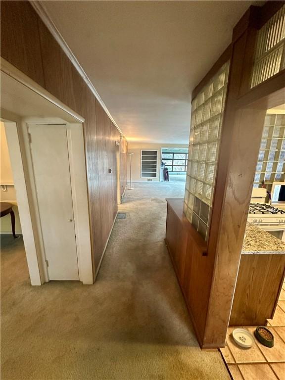 corridor with wooden walls, ornamental molding, and light carpet