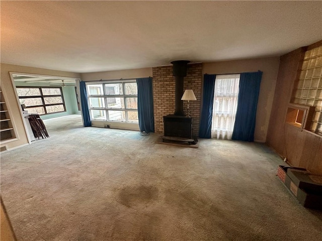 unfurnished living room featuring built in features, a textured ceiling, a wood stove, and carpet floors