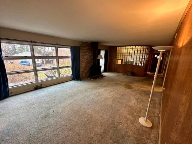 unfurnished living room with a wood stove, carpet, and visible vents