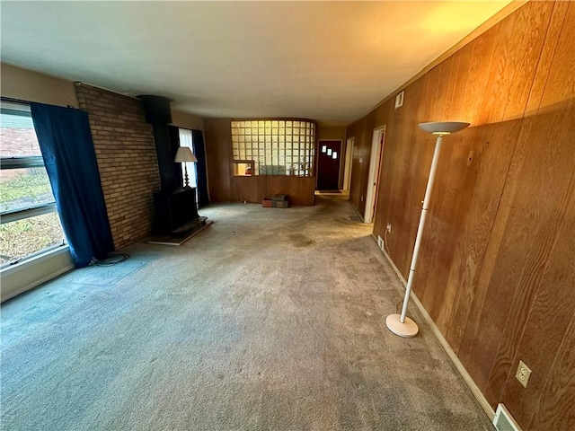 unfurnished living room with visible vents, carpet, wood walls, and a wood stove