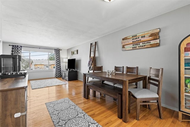 dining room with baseboards, arched walkways, and light wood-type flooring