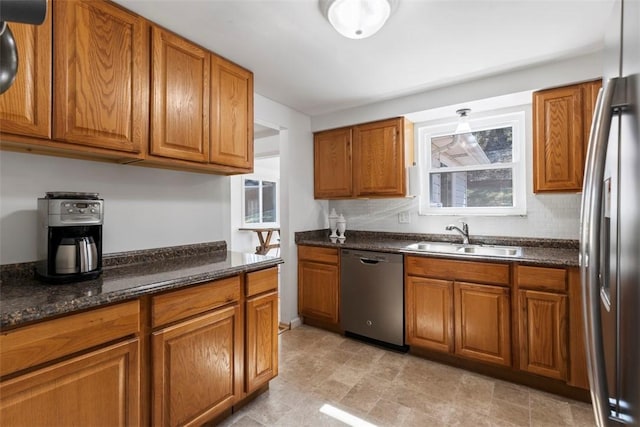 kitchen with decorative backsplash, dark stone countertops, brown cabinetry, stainless steel appliances, and a sink