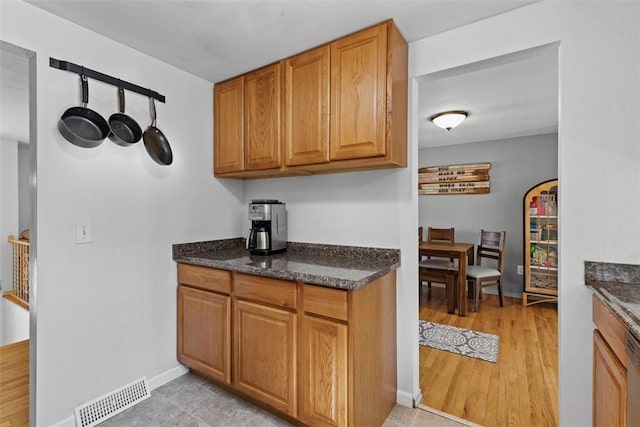 kitchen featuring brown cabinetry, visible vents, light wood-style flooring, and dark stone counters