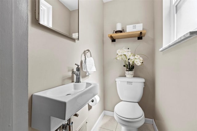 half bath featuring tile patterned floors, toilet, baseboards, and a sink