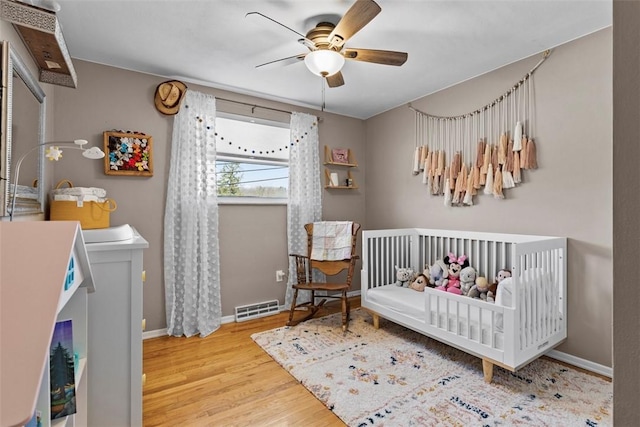 bedroom with visible vents, a ceiling fan, wood finished floors, a nursery area, and baseboards