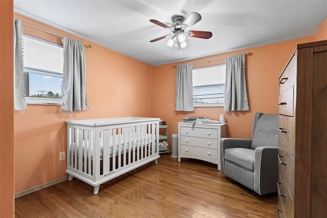 bedroom with ceiling fan, baseboards, a crib, and wood finished floors