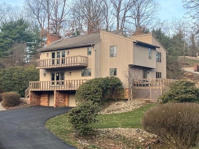 view of side of home with aphalt driveway, a chimney, and a balcony