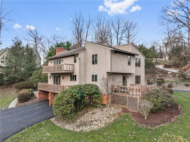 exterior space featuring a deck, a balcony, driveway, and a chimney