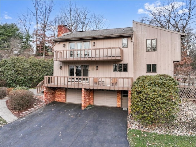 exterior space with a garage, driveway, a balcony, and a chimney