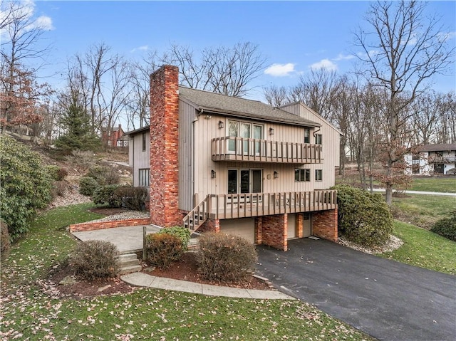 back of property with a balcony, a chimney, a garage, aphalt driveway, and a lawn