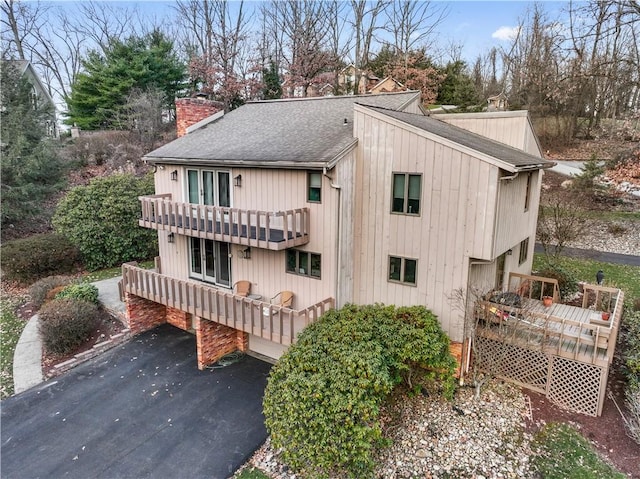 exterior space featuring aphalt driveway, a chimney, a deck, and a shingled roof