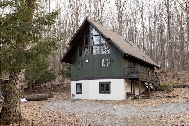 exterior space with a wooden deck, stairway, driveway, and a shingled roof